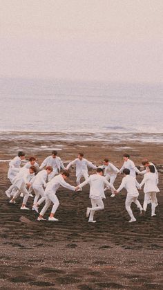 a group of young men in white suits dancing together on the beach near the ocean