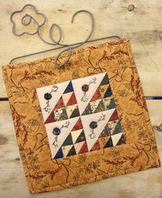 a quilted wall hanging with scissors on it's side and an ornament in the middle