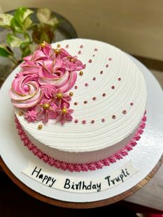 a birthday cake decorated with pink flowers on a white plate next to a potted plant