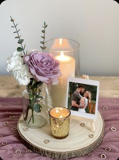 a candle and some flowers on a table with a picture frame next to it that is sitting on a wood slice