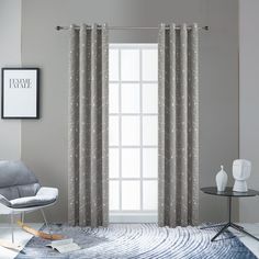 a living room filled with furniture and a window covered in grey drapes, next to a white chair