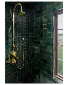 a green tiled bathroom with gold shower head and hand held shower faucet in the corner