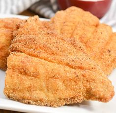 three pieces of fried chicken on a white plate with dipping sauce in the back ground