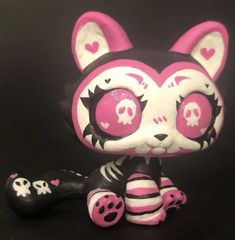 a pink and white cat figurine sitting on top of a black surface next to a bone