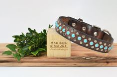 a brown leather dog collar with turquoise stones on it and a wooden plaque that says madison & made