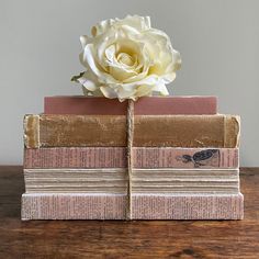 a white rose is sitting on top of several books stacked on each other, with one flower in the middle