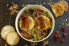 two fried eggs on top of a salad next to sliced tomatoes and other food items