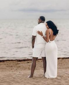 a man and woman standing on top of a sandy beach next to the ocean,