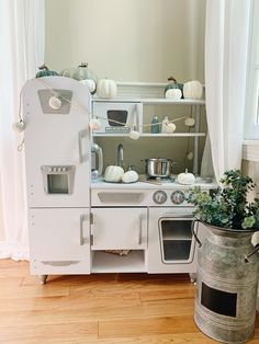 an old fashioned kitchen with white appliances and pumpkins on the windowsill, along with a potted plant