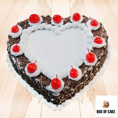 a heart - shaped cake with cherries on top sits on a wooden table in the shape of a heart