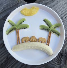 a white plate topped with banana slices and kiwis cut in the shape of palm trees