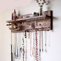 a wooden shelf with many necklaces hanging from it's sides and two vases filled with flowers