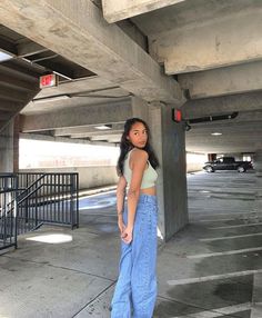 a woman standing under an overpass with her hands in her pockets and looking at the camera