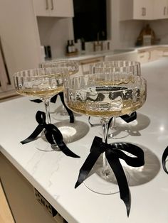 four wine glasses with black bows on them sitting on a counter top in a kitchen