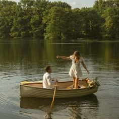 two people in a small boat on the water with trees in the backgroud