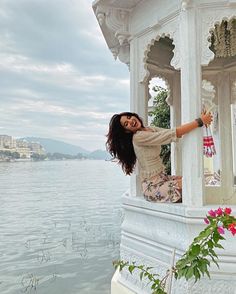 a woman standing on top of a white gazebo next to the ocean with flowers