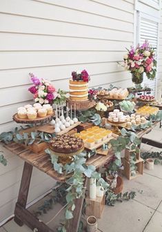 a table filled with cakes and cupcakes on top of wooden boards next to a building