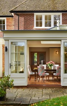 a dining room table and chairs in front of a brick building with french doors open