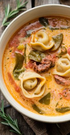 a white bowl filled with pasta and meat soup on top of a wooden table next to a spoon