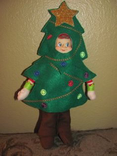 a green christmas tree doll with a gold star on its head and legs, standing in front of a wall