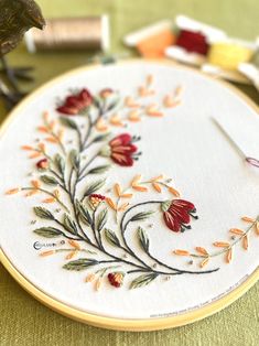 a bird sitting on top of a wooden table next to a embroidery hoop with flowers