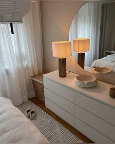 a white dresser with two lamps and a mirror in the corner next to a bed