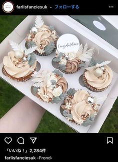 cupcakes with frosting and flowers in a box on the grass, being held by a person