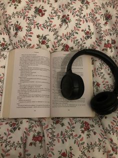 an open book with headphones on top of it sitting on a floral bed spread