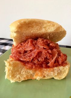 a sandwich with meat and cheese on a green plate sitting on a checkered tablecloth