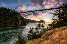 a bridge that is over some water with trees on the side and clouds in the sky