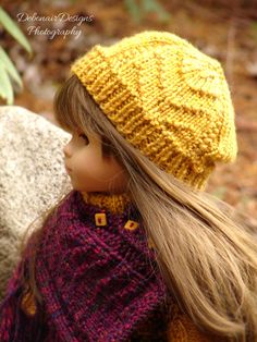 a close up of a doll wearing a knitted hat and scarf with long hair