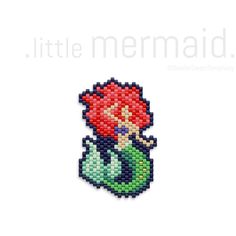 the little mermaid beaded brooch is sitting on top of a white surface and has a red flower in it's hair