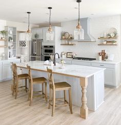 a kitchen with white cabinets and marble counter tops, two stools at the island