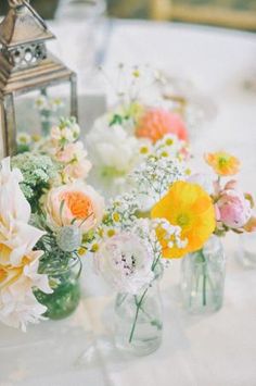 several vases with flowers are sitting on a table next to a small lantern light