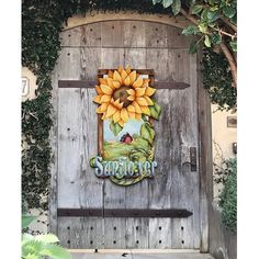 a wooden door with a sunflower painted on the front and side panel, surrounded by greenery