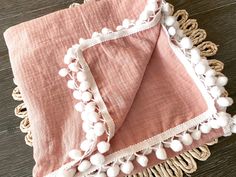 a pink and white blanket with pom poms on the edge sitting on a wooden table