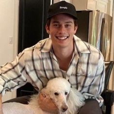 a man sitting in a chair holding a white poodle and smiling at the camera