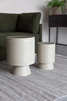 two white tables sitting on top of a carpeted floor next to a green couch