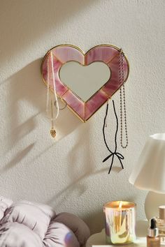 a heart shaped mirror hanging on the wall next to a night stand with a candle