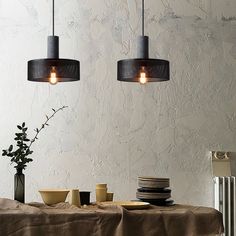 two pendant lights hanging over a table with plates and cups on it in front of a wall