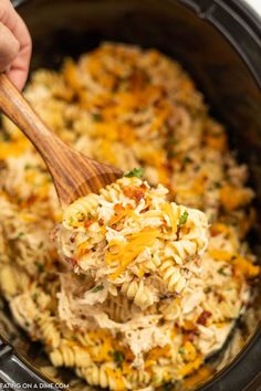 a wooden spoon full of macaroni and cheese being scooped from the crock pot