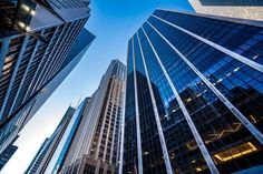 tall buildings are seen in the city at dusk, looking up into the blue sky