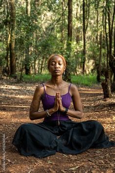 a woman sitting in the middle of a forest doing yoga