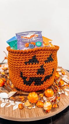 a crocheted pumpkin basket with candy and candies in it sitting on a table