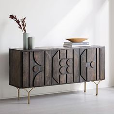 a wooden sideboard with metal legs and a bowl on it's top, in front of a white wall