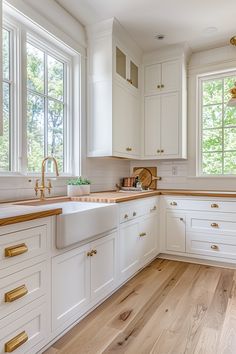 a kitchen with white cabinets and wood floors, gold handles on the faucets