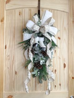 a christmas wreath hanging on the side of a wooden door with bells and pine cones