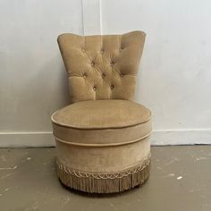 a round chair with fringe trim around the back and foot rests against a white wall