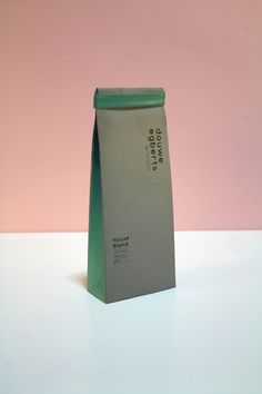 a green bag sitting on top of a white table next to a pink wall and a black cat