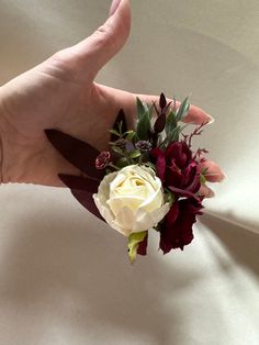 a person's hand holding a white and red boutonniere with flowers